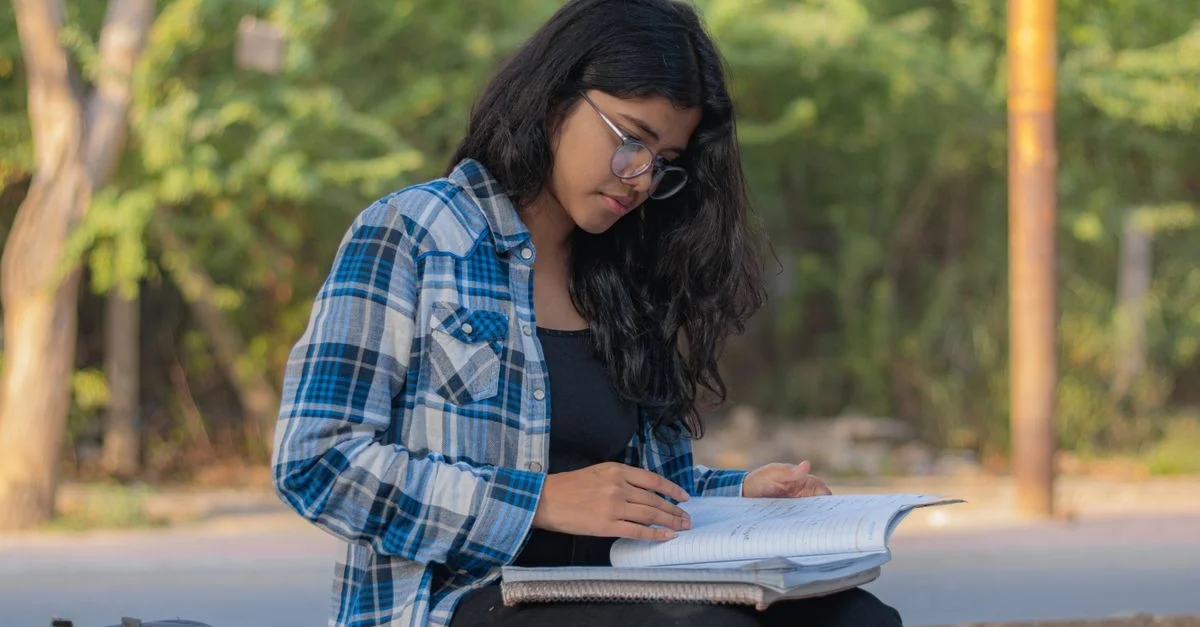 Jeune femme lisant et étudiant avec un carnet en plein air par une journée ensoleillée.
