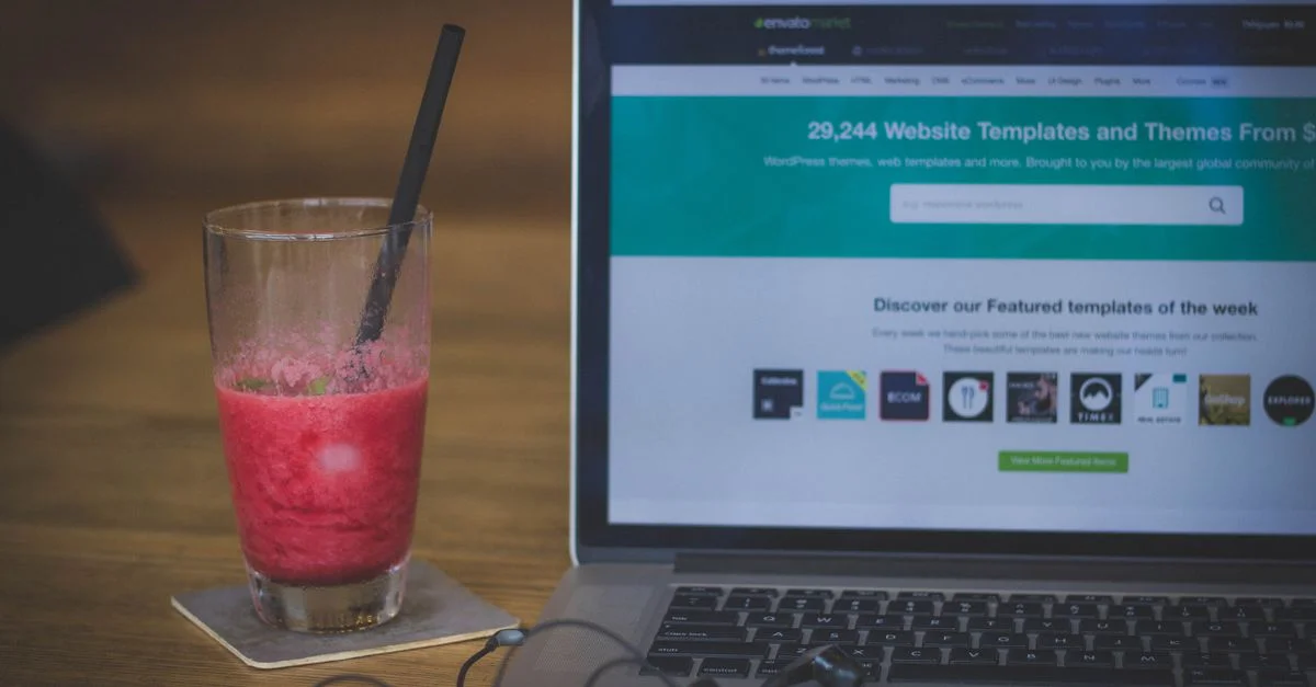 Un milkshake sur un bureau à côté d'un ordinateur portable affichant un site web, alliant travail et rafraîchissement.