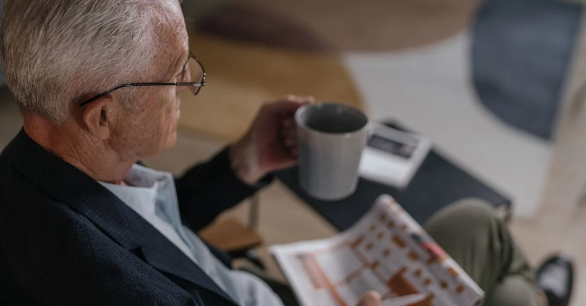 Homme senior savourant un café tout en lisant un journal à l'intérieur, dégageant calme et détente.