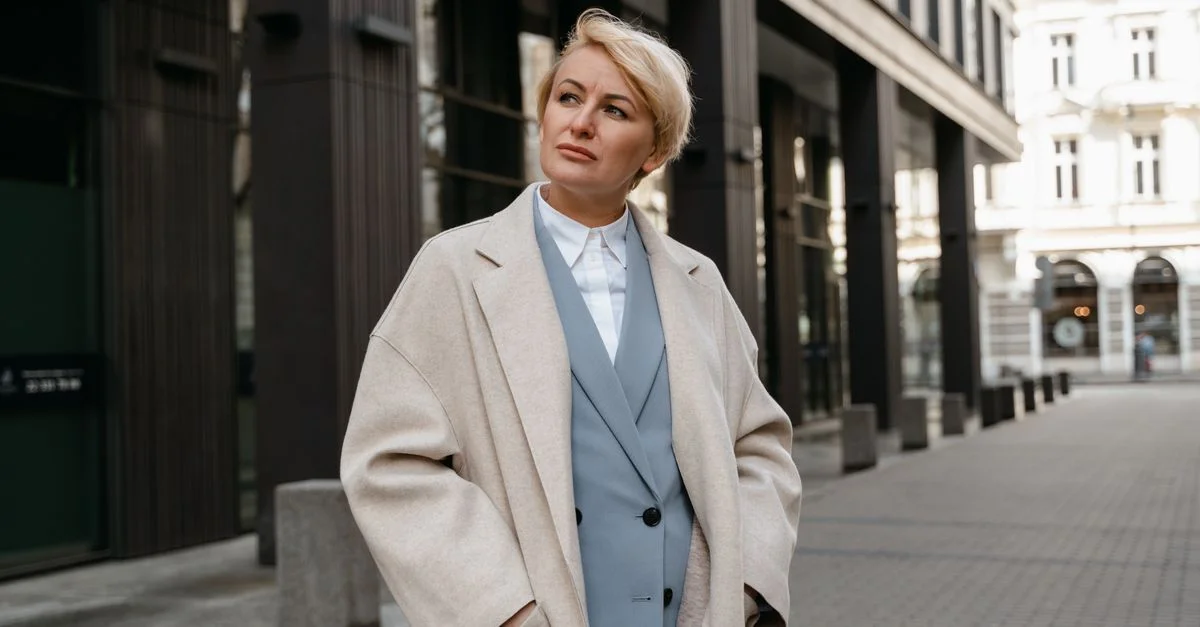 Femme d'affaires confiante en manteau beige se tient dans une rue moderne.