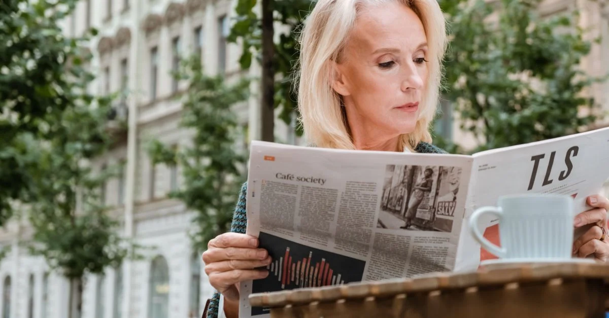 Femme mûre profitant d'une matinée d'été en lisant un journal dans un café en plein air à Saint-Pétersbourg.