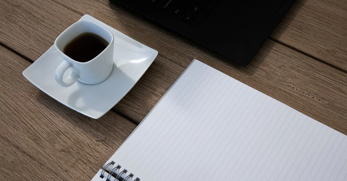 Tasse de café à côté d'un carnet ouvert sur un bureau en bois, parfait pour des images d'espace de travail.