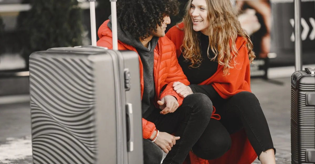 Couple souriant assis avec des bagages, profitant de leur voyage ensemble dans des tenues rouges vives.