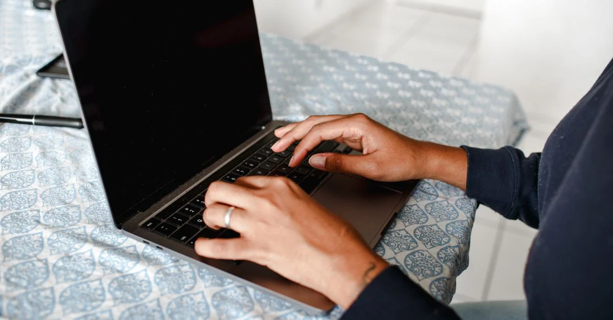 Gros plan sur des mains tapant sur un ordinateur portable à l'intérieur, sur une nappe à motifs.
