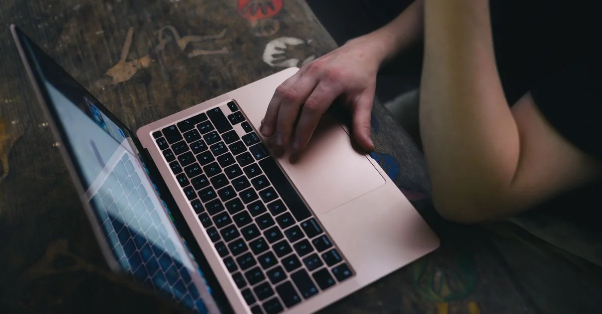 Un adulte utilise un ordinateur portable sur un bureau en bois rustique, offrant une ambiance de lieu de travail confortable.